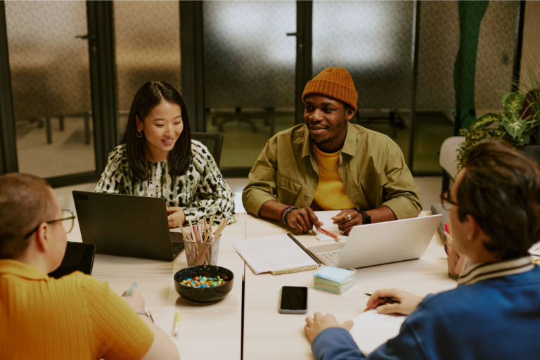 A multi-racial group of Gen Z employees discuss work at a collaborative meeting| Corporate Synergies