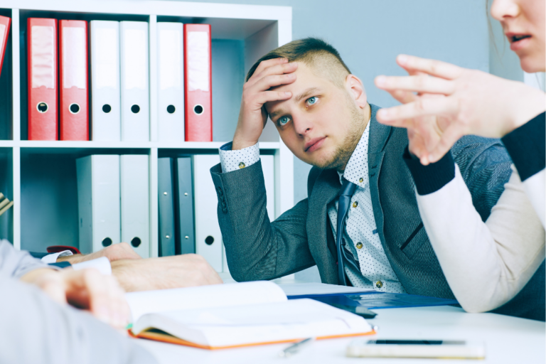 Disengaged employee holds his head while staring at a colleague during a meeting | Corporate Synergies